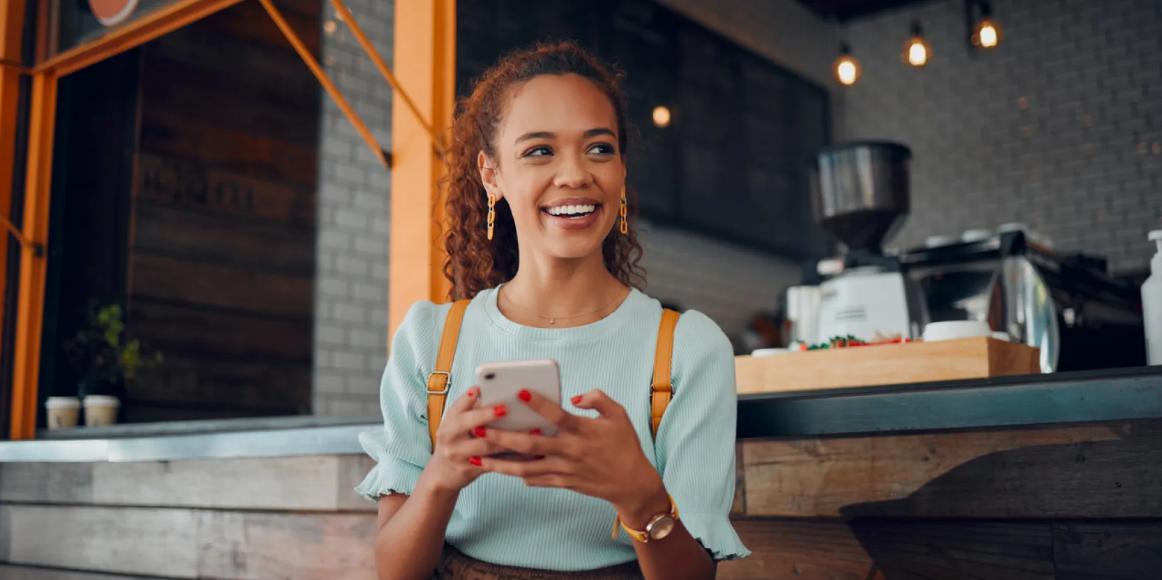 How to Build Wealth in Your 20s - Woman holding her phone in a coffee shop