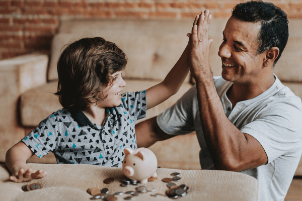 A dad and his child high-five after depositing money in a piggy bank