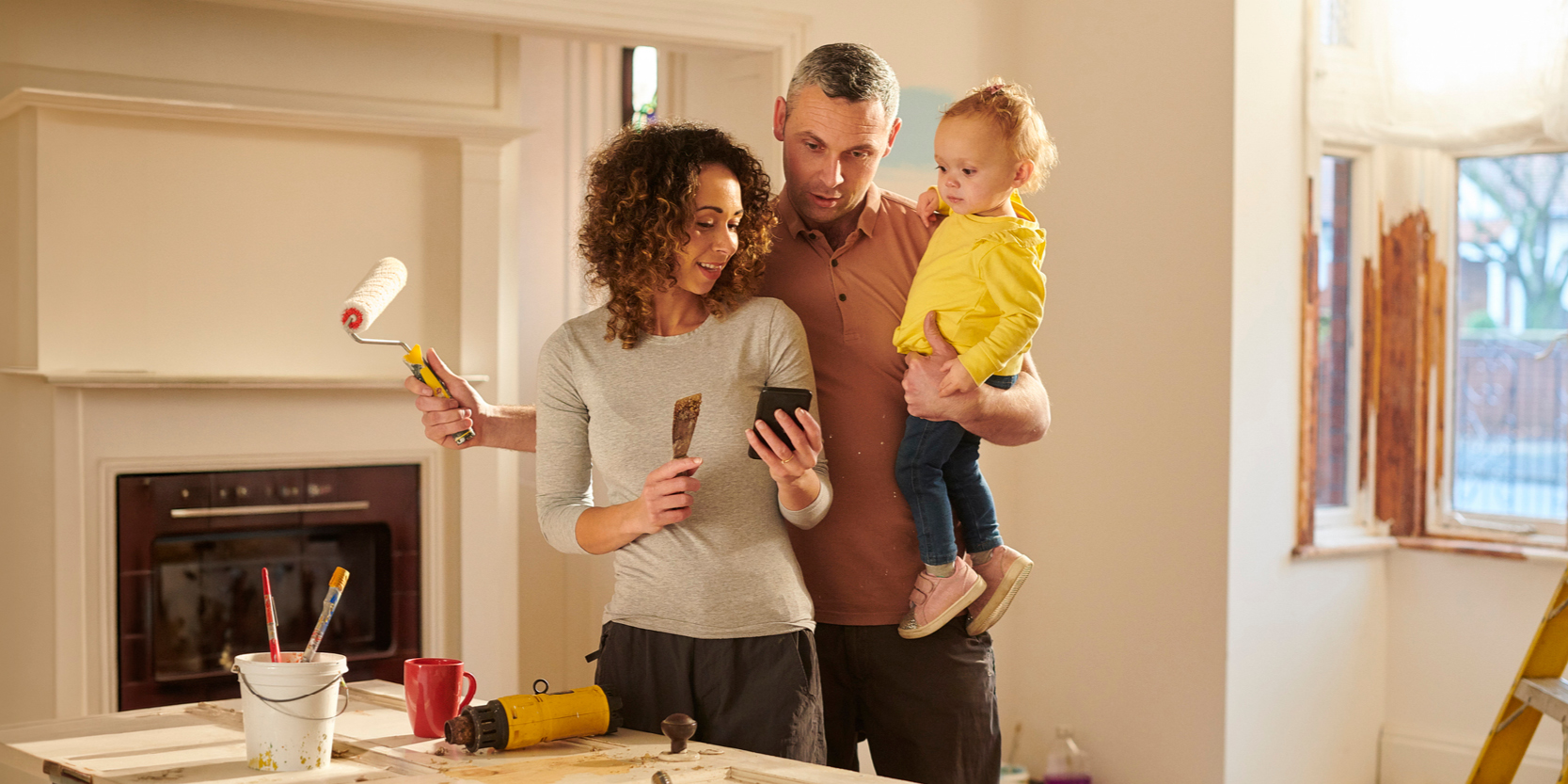 Family standing in their living room with paint supplies, smiling at a phone