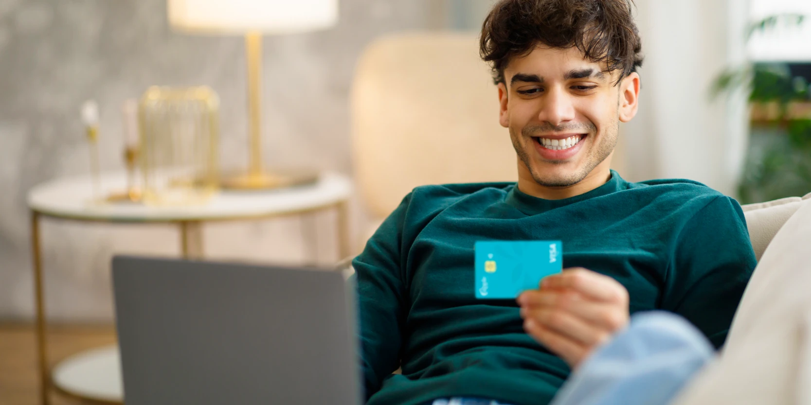 Student Credit Card vs Regular Credit Card: Man sitting on couch smiling at student credit card